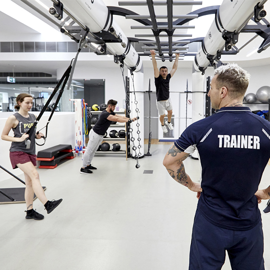 Group of people doing different workouts on the outrace machine with a trainer supervising